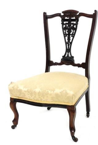 An Edwardian walnut nursing chair, with a pierced carved splat, padded seat on cabriole legs with castors.