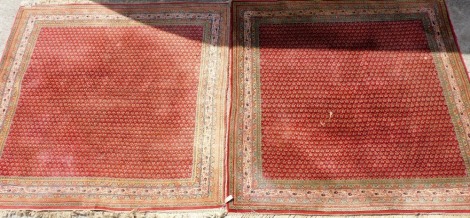 A pair of Pakistani red ground rugs, decorated with a central repeating floral motif, within repeating floral borders, 200cm x 200cm.