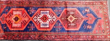 A Persian Hamadan runner, on a red and blue ground, 278cm x 103cm.