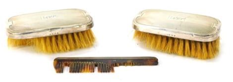 An Elizabeth II travel dressing table set, comprising two silver backed brushes with engine turned design and central crest stamped TFP, and a comb, Birmingham 1964, in fitted case. (AF)