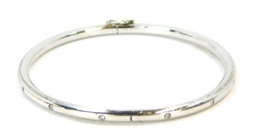 An 18ct white gold diamond set hinged bangle, set with fourteen tiny diamonds, safety clip clasp, 6cm diameter, 9g all in.