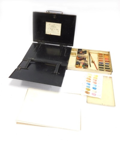 An E Wolff and Son artist's tin travelling paint box, the hinged lid enclosing an easel with adjustable strut support, the base with a drawer containing loose watercolour palettes of varying colours, 26cm wide.