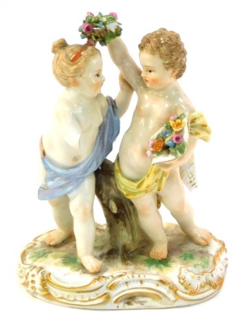 A 20thC Meissen figure group of two cherubs, fighting over a garland, polychrome decorated with gilt scroll highlights, 14cm high.