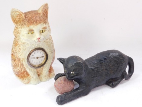 A late 19thC/early 20thC Bretby black painted terracotta model of a cat, with a ball of string, impressed mark down the side, design no 1518, 25cm wide, and a German porcelain cat shaped clock. (2)