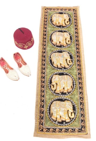 Eastern inspired wares, comprising a pair of Eastern leather embroidered shoes, a fez with gilt highlights and an embroidered elephant hanging panel with five circles, each with sequined elephant centre, 130cm x 40cm. (4)