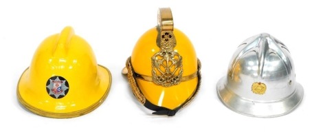 Three Fire Fighters helmets, comprising a mustard yellow and gilt scroll top helmet, a steel Fire Brigade helmet, and a Hampshire Fire Brigade yellow helmet. (3)