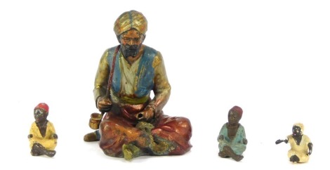 Four Bergman style cold painted metal figures, comprising a man with pipe sat with crossed legs, 8cm high, and three miniature figures, each 2.5cm high. (4)