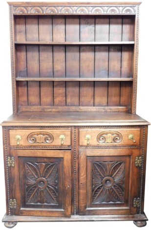 A carved oak dresser, the raised back with fan detail above two drawers and two cupboards, on bun feet, 88cm high, 104cm wide, 54cm deep.