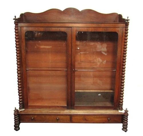 A Victorian rosewood bookcase, with a shaped tray top, on fluted and moulded column supports, with two large two sectioned astragal glazed doors, with shelves above two drawer base, terminating in bobbin finials, 200cm high, 174cm wide, 55cm deep. Note: V