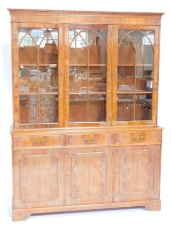 A 20thC yew wood bookcase, with a dentil carved cornice above three astragal glazed doors, with three drawers and three cupboards on bracket feet, 190cm high, 145cm wide, 40cm deep.