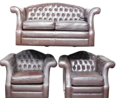 A brown leather Chesterfield style suite, comprising two seater sofa and two matching armchairs, each with brown button back and stud detail, the sofa 136cm wide, 87cm deep, 50cm high, the armchairs 98cm wide, 87cm deep, 90cm high. (3) The upholstery in t