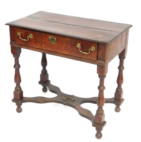 An 18thC oak side table, with two planked top above single drawer, with brass escutcheon and handles, on H frame base on bun feet, 67cm high, 71cm wide, 42cm deep.