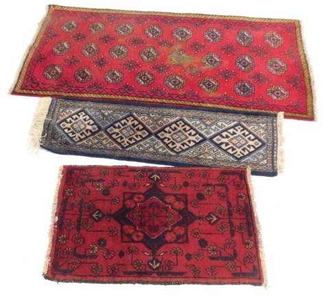 Three rugs, comprising a red Eastern style medallion rug, 120cm x 64cm, a blue four medallion runner, 86cm x 30cm, and a red central medallion and flower design rug, 65cm x 44cm. (3)