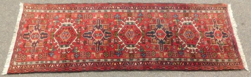 A Persian rug, with six central medallions on a red ground with multi coloured border, 196cm x 68cm.