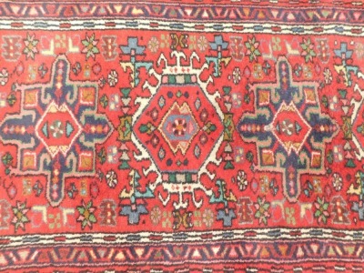 A Persian rug, with six central medallions on a red ground with multi coloured border, 196cm x 68cm. - 2