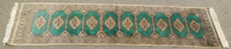 An Afghan or Pakistani runner, with ten guls, on a green and cream ground, with pink borders, 252cm x 62cm.