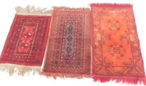 Three rugs, comprising one with two central medallions, on a red ground, 59cm x 44cm, a rug with two central medallions on orange ground, 88cm x 48cm, and a rug with three medallions on red orange ground, 78cm x 46cm. (3)