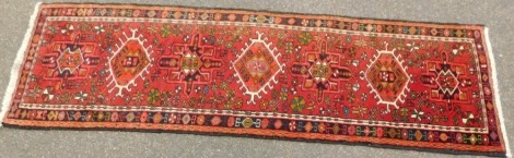 A Persian runner, with six central medallions on a red multi coloured ground, 196cm x 63cm.