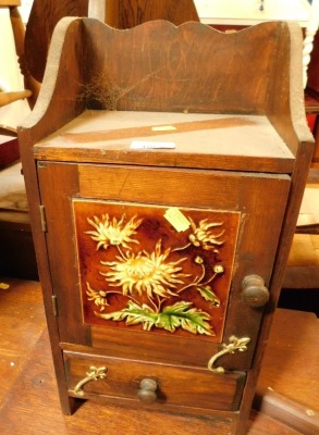 An oak smokers cabinet, with majolica tile insert decorated with sunflowers.