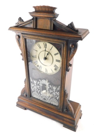 An early 20thC oak stained architectural mantel clock, with 13cm diameter dial stencilled with Roman numerals, with a glazed door decorated with arches and flowers, on compressed feet with eight day movement, 49cm high.