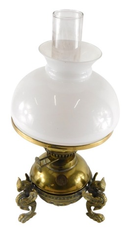 An early 20thC brass oil lamp, with clear glass chimney, milk glass shade and brass reservoir, stamped Use Only Paraffin, on elaborate griffin feet, 47cm high.