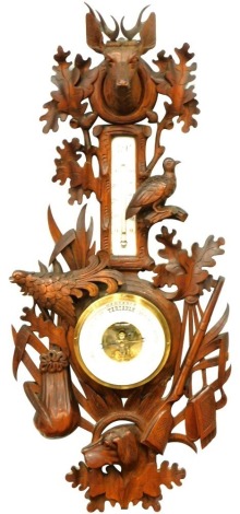 An early 20thC Black Forest barometer and thermometer, heavily carved with stag finial, with partridge leaves and ferns, with 12cm diameter dial and enamel thermometer, 73cm high.