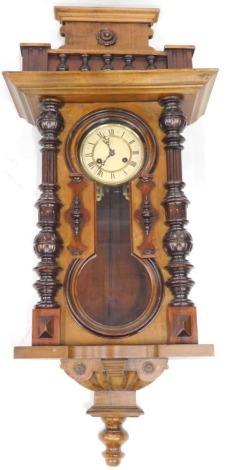 A 19thC walnut Vienna wall clock, the 13cm diameter Roman numeric dial stamped Junghans, flanked by quarter columns and fronted by a figure of a glass, surmounted by columns and a floral patera, in a shaped case, 76cm high.