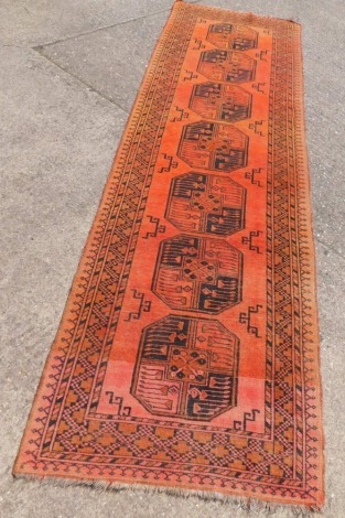 An Afghan runner, with a design of medallions on orange ground with multiple borders, 299cm x 92cm.