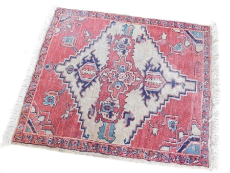 A Persian rug, with a central pole medallion in orange with a cream ground, with spandrels, bearing inscription, 84cm x 81cm.