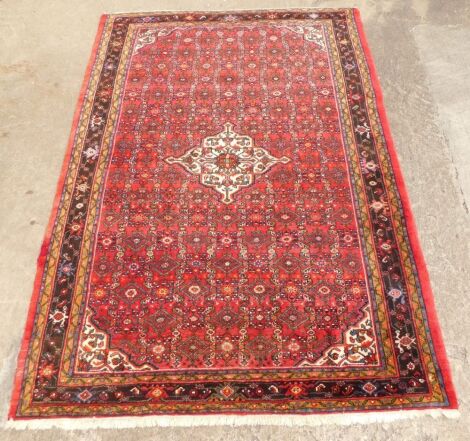 A Persian carpet, with an all over design of roundels and other geometric devices, on a red ground, 311cm x 213cm.