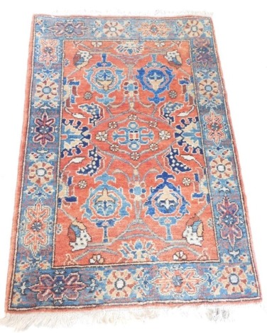 A Persian rug, with a design of medallions in blue and pale blue on a red ground with one wide border, 115cm x 78cm.