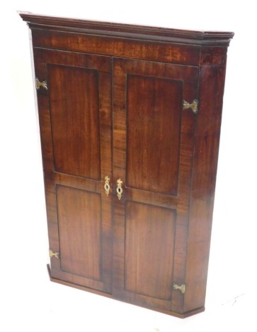 A George III hanging corner cabinet, with a moulded cornice above two panelled doors, each with elaborate brass handles and escutcheons, 119cm high, 87cm wide.