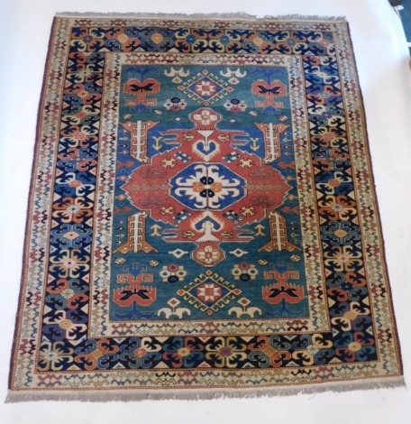 A Persian Kazak style rug, with a design of multicoloured lozenges and medallions on a green ground, one wide, two narrow borders, 198cm x 171cm.