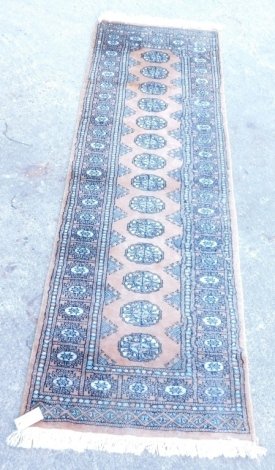 A Pakistani Afghan runner, with a Bokhara design on a gold ground, 193cm x 60cm.