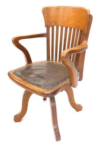 An early 20thC oak office chair, with a slatted back and a padded seat, on four splayed legs.