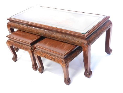 A nest of three oriental hardwood tables, each carved with figures, trees, etc. on shaped supports, the largest 107cm wide, the smallest 37cm wide.