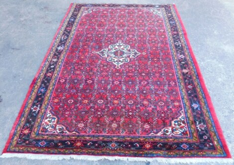 A Persian carpet, with an all over design of flowers, geometric devices on a red ground, with one wide, two narrow borders, 305cm x 217cm.