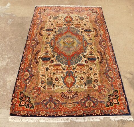 A Persian rug, with a central medallion, in pale blue, orange, beige, on a cream ground with spandrels, 306cm x 198cm