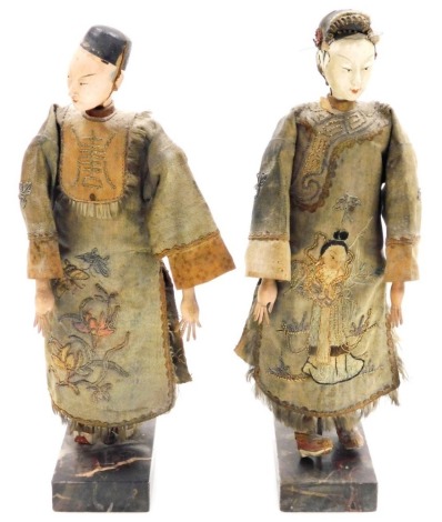 Two Oriental figures, with pottery faces and embroidered clothing, on plinths, each 29cm high. (AF)