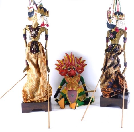 A pair of Eastern puppet figures, with articulated limbs on wooden bases, profusely decorated in colours, 66cm high, and a further puppet with stringing. (3)