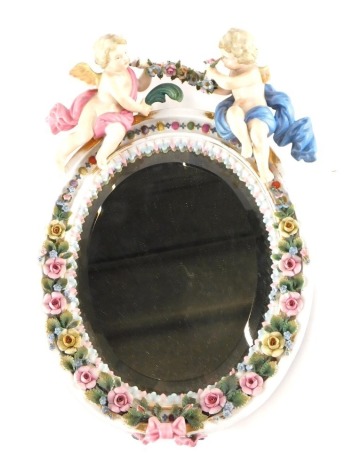 A Dresden style porcelain hanging mirror, of oval form with bevel glass surmounted by two cherubs holding garland, with a further garland surround with ribbon, predominantly in pink, green and blue, unsigned, 29cm high.