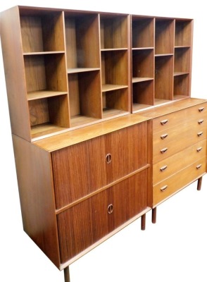 Two pieces of mid century teak lounge furniture, comprising a chest of five graduated long drawers, with an upper structure of open recesses, raised on turned legs, 170cm high, 90cm wide, 48cm deep, and a double tambour fronted cupboard enclosing shelves,