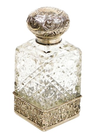 An Edward VII cut glass and silver mounted scent bottle, the lid embossed with flowers and scrolls, the bottle of rectangular form with stopper, on a white metal pierced base decorated with scrolls and flowers, London 1903, 14cm high.