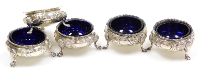 Five Victorian silver circular salts, embossed with flowers and leaves and monogram engraved cartouches, each raised on three hoof feet, one lacking blue glass liner, dates for London 1857 and 1867, weighable silver 10.52oz.