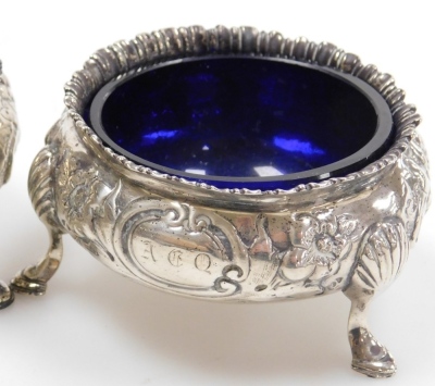 Five Victorian silver circular salts, embossed with flowers and leaves and monogram engraved cartouches, each raised on three hoof feet, one lacking blue glass liner, dates for London 1857 and 1867, weighable silver 10.52oz. - 2