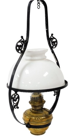 An early 20thC brass hanging oil lamp, in a scrolling cast iron frame, with glass chimney and white glass shade, 72cm high.