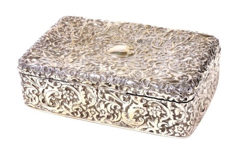 A Victorian silver dressing table box, of rectangular form, embossed with flowers, scrolls, and a vacant cartouche, the interior enclosing a removable treen liner, George Nathan and Ridley Hayes, Birmingham 1894, 6.5cm high, 22cm wide, 13cm deep.