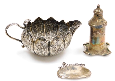 An Indian white metal jug, with petallated rim and repousse decorated with flowers, shaped snake handle, 11cm wide, a silver decanter label, engraved Jeff's Scotch, marked 925, and a silver pepper pot.