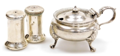 A George V silver mustard pot, with a shaped handle with applied acanthus leaf decoration, raised on three leaf cast scroll legs, the hinged lid enclosing a blue glass liner, London 1929, and a pair of George V silver salt pots, Birmingham 1915, weighable