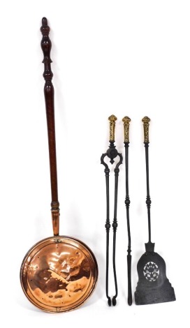 A set of Victorian cast iron fire implements, with foliate embossed brass handles, comprising shovel, poker and pair of coal tongs, 75cm high, together with a copper warming pan with a turned wooden handle, 114cm high. (4)